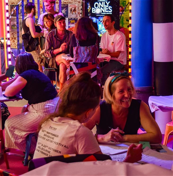 A photo of a tour ready session with people meeting each other in a brightly coloured room. They're sitting at tables and smiling and talking to each other.