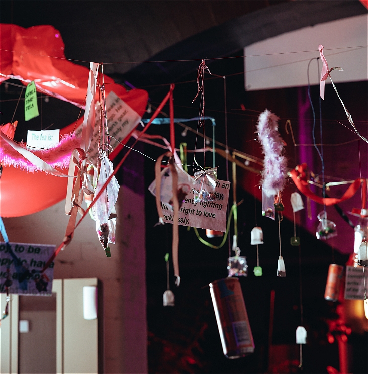 An image of recycled materials hanging from the ceiling, there is paper notes, tinsel, cans, tea bags, and bits of string dangling form the roof.